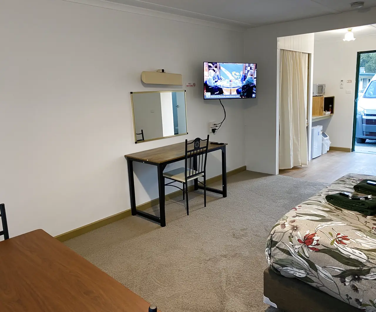 Motel room with a desk, wall mounted television and queen bed
